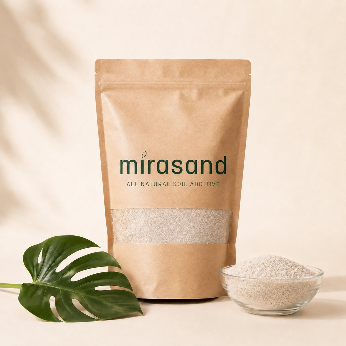 Mirasand kraft pouch on a cream background with a monstera leaf and a bowl of white mineral soil topper